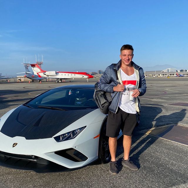 Stephen Deleonardis in a white t-shirt, blue jacket, and black shorts in front of his Lamborghini Huracan.